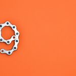 A metal chain shaped like the number nine against a vibrant orange background with copy space.