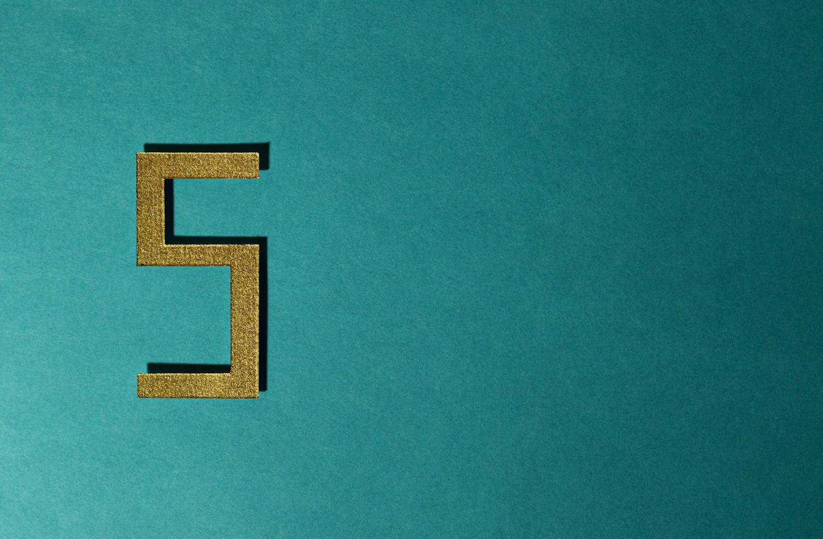 Abstract photo featuring a golden number five on a teal background with negative space.